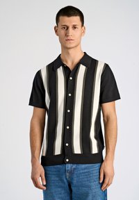 Svart och vit kortärmad skjorta med vertikala ränder, med spetsig krage och knappstängning fram, bärs med blå jeans.