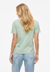 Gaišzaļš kokvilnas T-krekls ar īsām piedurknēm un taisnu piegriezumu; kombinēts ar augsta vidukļa ziliem džinsiem. Minimālistisks dizains bez redzamām rakstēm.