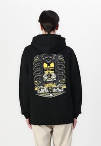Black hoodie with a large, colorful graphic on the back featuring a detailed design with yellow, black, and white elements, and embroidered accents.