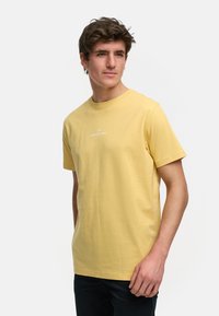 Gul bomull t-skjorte med korte ermer, rund hals, og en trykt logo på brystet. Glatt tekstur og vanlig passform.