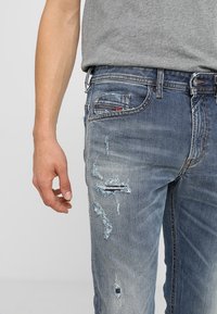 Ljust blå denimjeans med slitna detaljer, inklusive revor och fransar. Knapp- och dragkedjestängning med sidofickor och bakfickor.