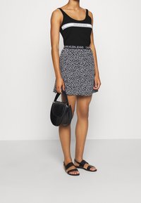 Černý top na ramínka Calvin Klein s bílým logem, sukně s květinovým vzorem v černé barvě, černá crossbody taška a černé ploché sandály.