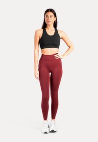 Zwarte sportbeha met racerback-ontwerp en gevoerde cups, gecombineerd met bordeauxrode hoge taille legging met zijzakken en een gladde textuur.