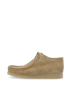 Beige ruskindssko, lav profil med rund tå, snøring foran og tekstureret gummisål. Minimalistisk design med dekorativ syning.