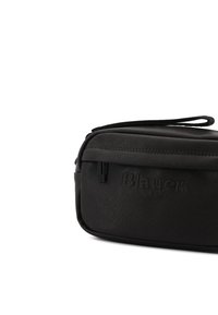 Borsa rettangolare nera realizzata in materiale testurizzato. Presenta una chiusura con zip, un manico intrecciato e un marchio in rilievo sulla parte anteriore.