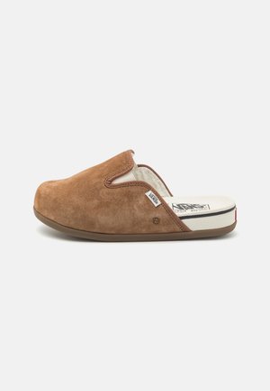 Brown suede slipper with a closed back, soft lining, and a rubber sole. Features a stitched trim and a logo tag on the side.