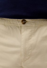Beige shorts med knaplukning og elastisk talje, lavet af glat stof; har en sidesøm og syningsdetaljer.