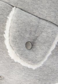 Γκρι υφασμάτινη τσέπη με κούμπωμα ασφαλείας και λευκή γέμιση φλις σε απαλό υφασμένο ένδυμα.