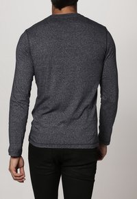 Pitkähihaisen harmaan t-paidan, joka on valmistettu neuloksesta, on normaali pyöreä kaula-aukko ja vartalonmyötäinen siluetti, jossa on sileä pinta eikä näkyviä kuvioita.