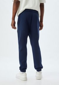 Joggers en color marino fabricados con un material suave, que cuentan con una cinturilla elástica y bolsillos laterales. Diseñados con piernas ajustadas y puños acanalados.