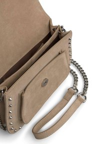 Beżowa zamszowa torebka crossbody z łańcuszkowym paskiem, zdobiona srebrnymi piramidowymi ćwiekami, z kieszeniami na zamek błyskawiczny oraz klapą zamykaną na magnes.