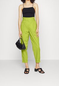 Limoengroene hoge taillebroek met een riem, zwarte getailleerde top, zwarte handtas met witte stiksels, en zwarte block-heel sandalen.