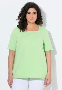 T-shirt verde chiaro a maniche corte con scollatura quadrata. Tessuto morbido e vestibilità ampia, abbinato a pantaloni bianchi. Senza motivi o decorazioni.