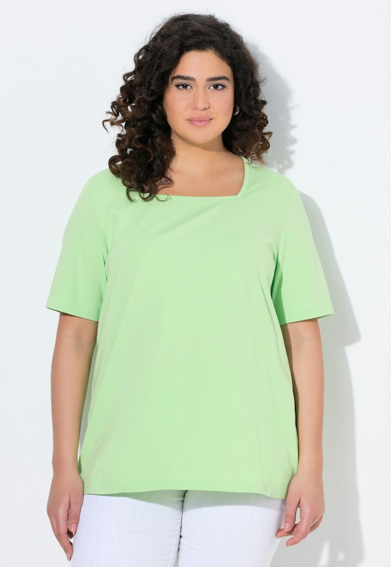 T-shirt verde chiaro a maniche corte con scollatura quadrata. Tessuto morbido e vestibilità ampia, abbinato a pantaloni bianchi. Senza motivi o decorazioni.