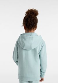 Ljusblå hoodie av mjukt tyg. Har en framficka och ribbade ärmslut. Slät textur med en avslappnad passform.