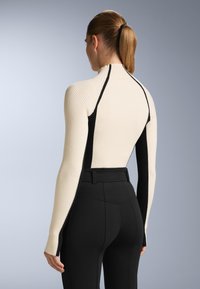 Žebrovaný dlouhý rukáv v krémové a černé barvě, s vysokým límcem a přiléhavým střihem, doplněný černými kalhotami s vysokým pasem.