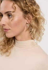 Beige high-neck top made of smooth fabric, featuring a decorative pattern on the collar and curly hair visible in profile.
