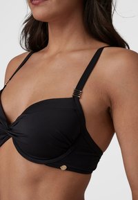 Černý bikiny top s designem s otočeným předním dílem. Obsahuje nastavitelné ramínka a detaily ve zlatém tónu. Hladká, elastická tkanina.
