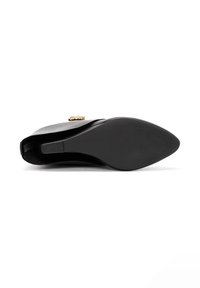 Botte noire en cuir jusqu'à la cheville avec un bout pointu, texture lisse et une touche dorée sur le côté. La semelle est plate avec un motif de semelle.