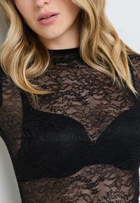 Body in pizzo nero con motivi floreali e design aderente, dotato di uno strato sottostante nero solido per copertura e colletto alto.