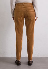 Corduroy broeken in een warme mosterdkleur met een slim fit, voorzien van twee achterzakken en een gladdere textuur. Details omvatten een hoge taille ontwerp.