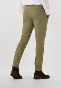 Pantalons slim-fit vert olive avec une texture lisse, dotés de poches latérales et arrière, portés avec des bottes en cuir marron.