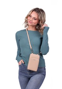 Beige crossbody taška s hladkým texturovaným povrchem, obsahující přední kapsu a nastavitelný popruh, nošená přes tyrkysový žebrovaný svetr.