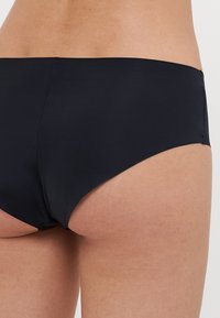Čierne plavky s elastického materiálu, s stredným pásom a hladkým povrchom, s čistými okrajmi a minimálnymi švami.