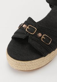 Schwarze Denim-Wedge-Sandalen mit einer strukturierten Espadrille-Sohle, zwei verstellbaren goldfarbenen Schnallen und einem weichen, geschwungenen Riemendesign.