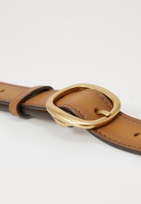Tan leather strap with brown accents, featuring a rounded gold metal buckle and visible stitching details. Marked with "Coach."
