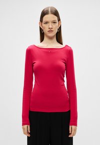 Majica s dolgimi rokavi iz svetle roza tkanine, z obliko čolnastega ovratnika in majhnim logotipom na prsih. Gladka tekstura in prilegajoč kroj.