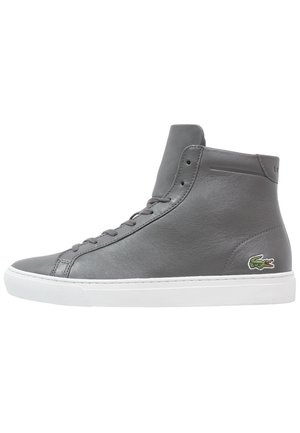 Szary skórzany sneaker z wysoką cholewką, białą podeszwą i zielonym logo krokodyla na boku pięty, przedstawiony na widoku z profilu.