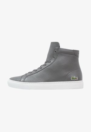 Szary skórzany sneaker z wysoką cholewką, białą podeszwą i zielonym logo krokodyla na boku pięty, przedstawiony na widoku z profilu.