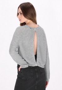 Grijze gebreide trui met een keyhole-design aan de achterkant en knoopaccenten. Lange mouwen en een losse pasvorm, gecombineerd met een zwarte denim rok.