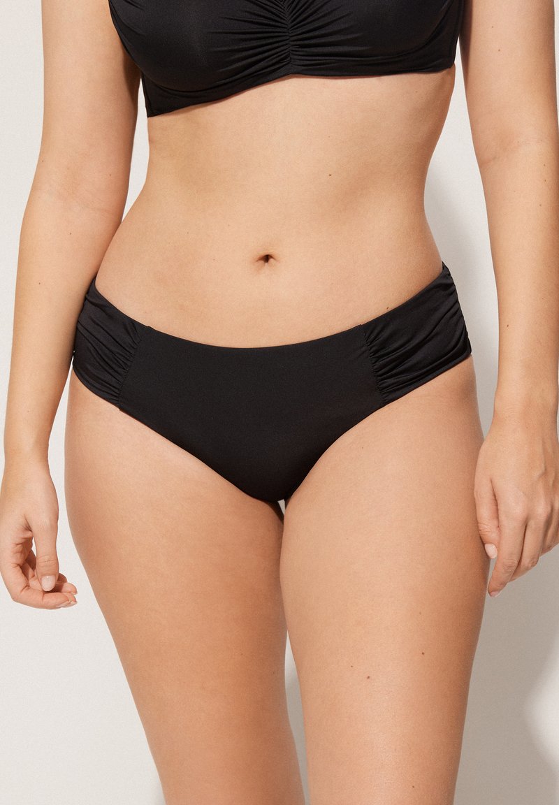 Černý bikini set s řaseným braletem a odpovídajícími spodními díly. Hladká látka s klasickým střihem a detailním bočním řasením.