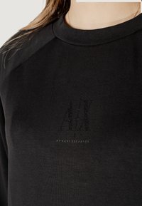 Felpa nera con collo a girocollo a coste, logo testurizzato "A/X" sul davanti e una morbida texture di tessuto liscia.