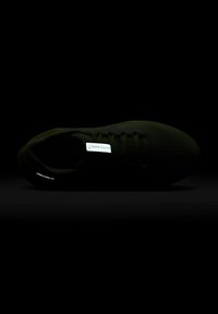 Chaussure de sport noire avec une tige texturée, dotée d'une étiquette réfléchissante Nike et d'un design épuré. La semelle est incurvée, améliorant les performances.