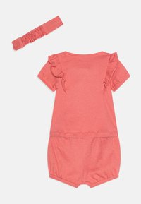 Une combinaison pour nourrissons de couleur corail rose avec des manches volantées, une taille élastique et un bandeau assorti. En coton doux et extensible avec une texture lisse.