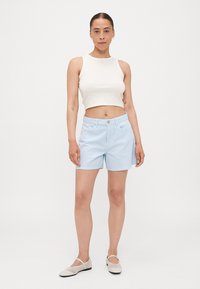 Shorts rayés bleu clair en coton, dotés d'une fermeture à bouton et à zip, de poches avant et d'une coupe décontractée. Accompagnés d'un top court blanc.