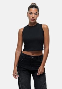 Top corto nero con collo alto e senza maniche, abbinato a jeans neri a vita alta con cuciture dettagliate.