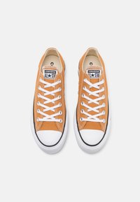 Oranžové plátěné tenisky s bílými tkaničkami, gumovou špičkou, černými pruhy po stranách a brandingem "CONVERSE ALL STAR" na jazyku.