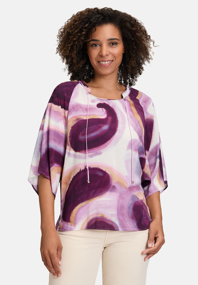 Farverig bluse med lilla og pink flydende mønstre. Løs pasform, brede ærmer, justerbar snorhætte, glat stoftekstur.