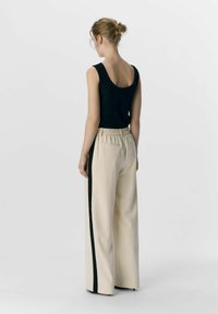 Top a coste nero con scollatura a gomito, abbinato a pantaloni larghi crema con bande laterali verde scuro e cintura elastica.