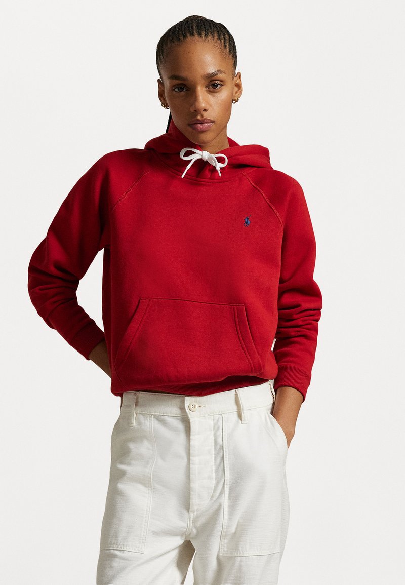 Rød hettegenser med en frontlomme og hvite snorer. Har en subtil blå logo på venstre bryst. Strukturert stoff, avslappet passform.