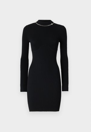 Zwart geribbelde lange mouw jurk met een bodycon pasvorm. Heeft een opstaande kraag en een zilveren kettingaccent bij de kraag. Zachte textuur.