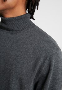 Pull à col roulé gris avec un col côtelé et une texture douce, présentant une coupe ajustée et des manches longues.