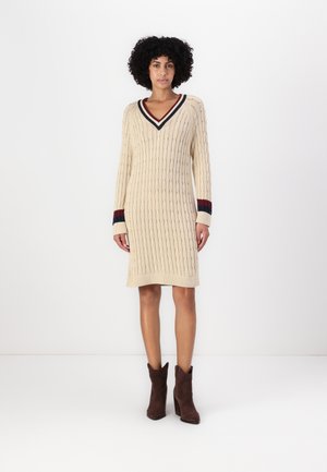 Beige gebreid sweaterjurk met een V-hals, voorzien van ribgebreide manchetten in marineblauw en bordeaux, aangevuld met een textuurpatroon door het hele ontwerp.
