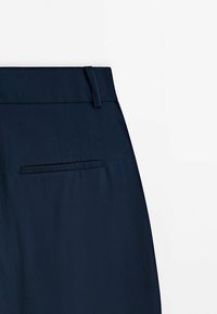 Pantalon bleu marine avec une ceinture plate, doté d'une poche arrière et d'une texture lisse. Design simple, adapté à une tenue formelle ou décontractée.