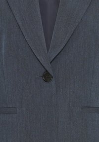 Blazer gris foncé à un bouton unique avec de larges revers et deux poches frontales horizontales de chaque côté.