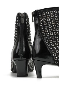 Czarne botki za kostkę z błyszczącym wykończeniem, zapinane na zamek z dużymi okrągłymi cekinami po bokach. Grube obcasy zapewniają stabilność.